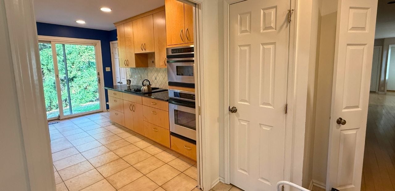 Before: Narrow galley kitchen in North Bethesda with maple slab (flat-panel) cabinets, black granite countertop, diamond-pattern tile backsplash, ceramic tile floor, and dark blue accent wall.